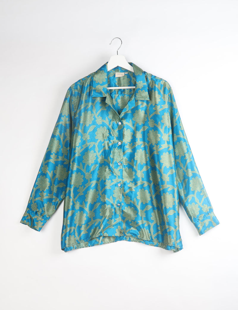 Blue floral resort shirt with long sleeves and button front, shown hanging on white hanger against white background