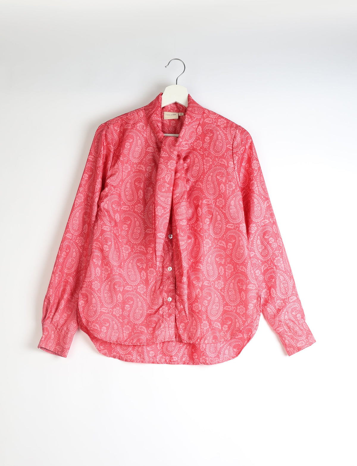 Pink paisley patterned long-sleeve button-up shirt with attached bowtie, hanging on white hanger, size M tag visible