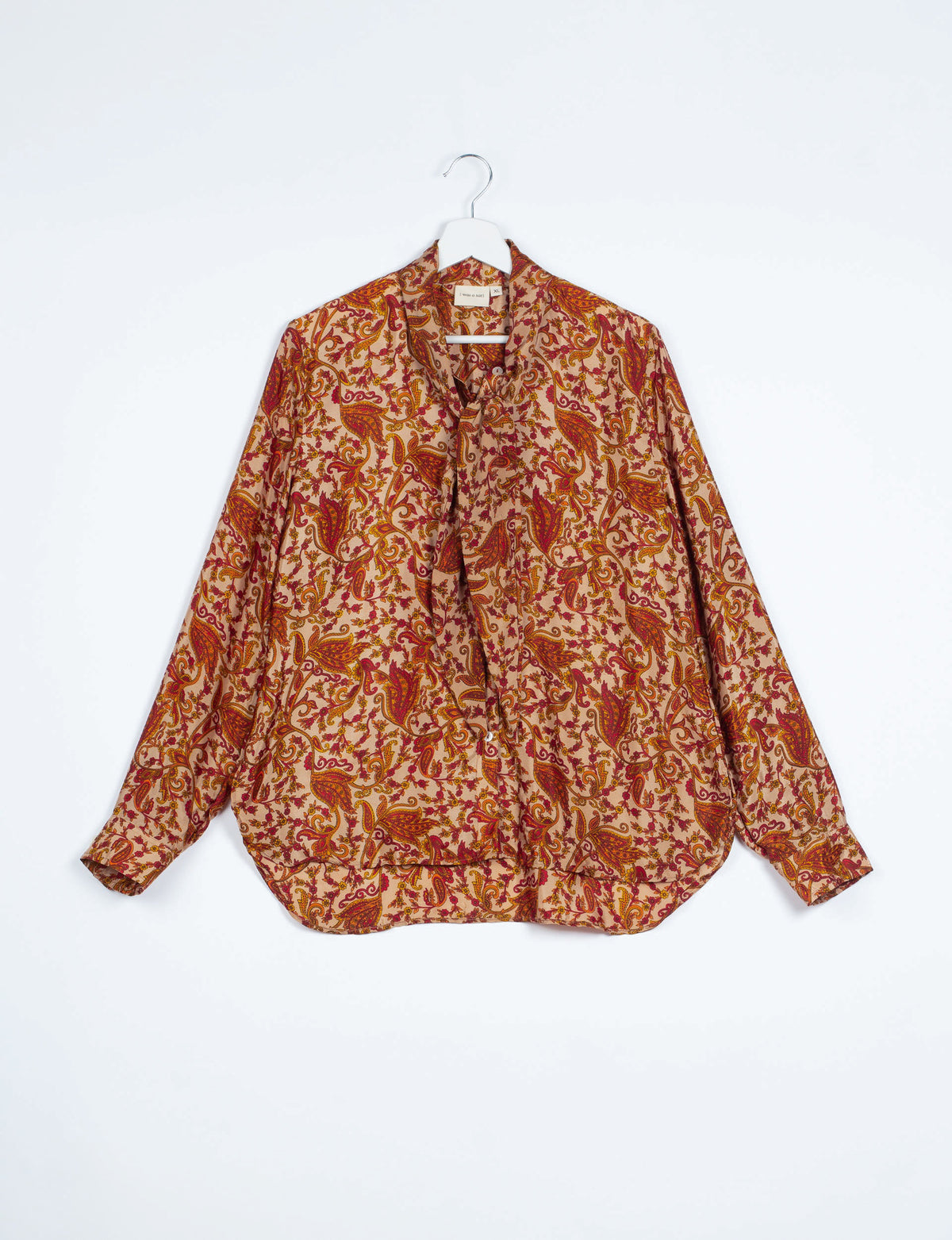 Long-sleeve button-up shirt with orange and red abstract floral paisley pattern, bowtie neckline, hanging on white hanger