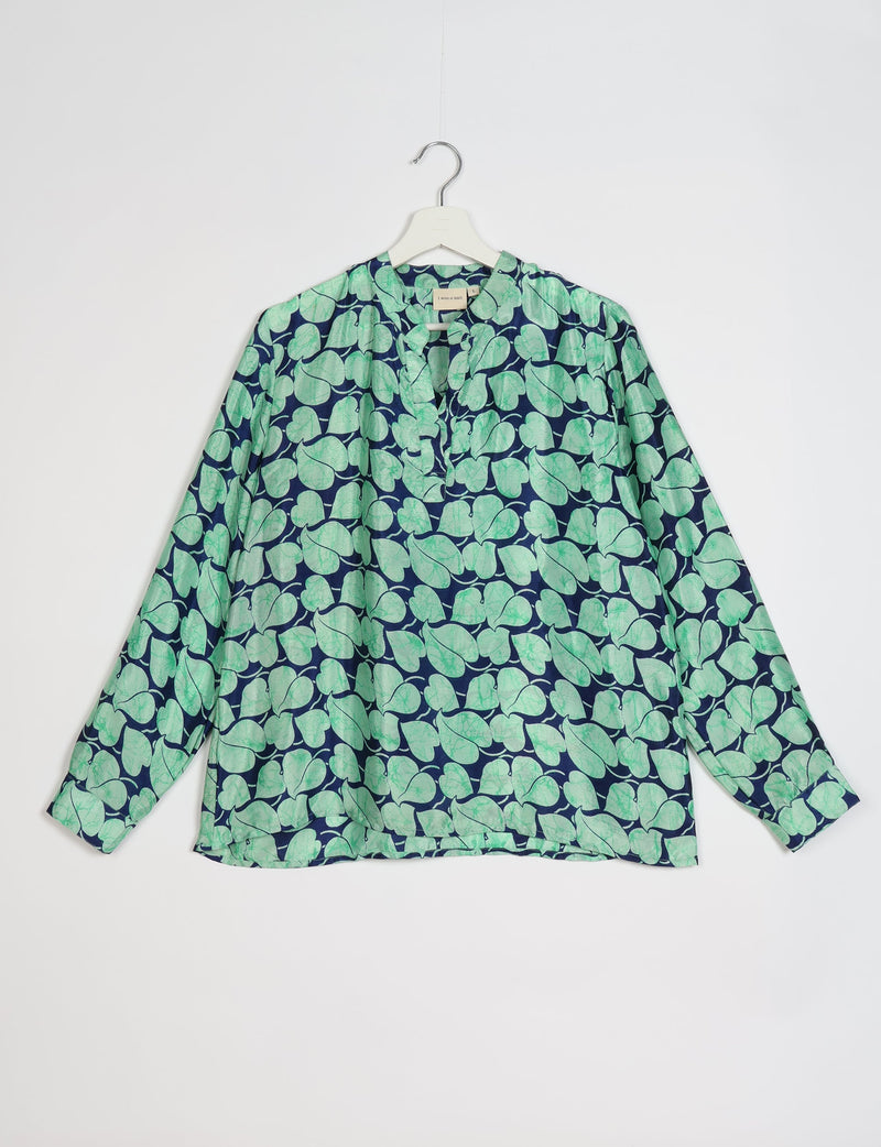 Long-sleeve blouse with blue background and green leaf pattern, V-neckline, hanging on white hanger against white background