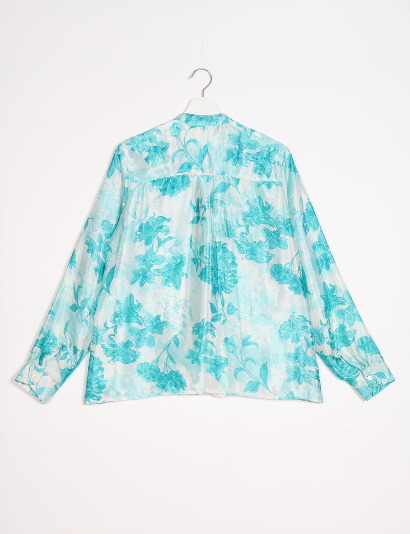 Blue floral patterned long-sleeve blouse with buttoned cuffs hanging on white hanger, back view on white background