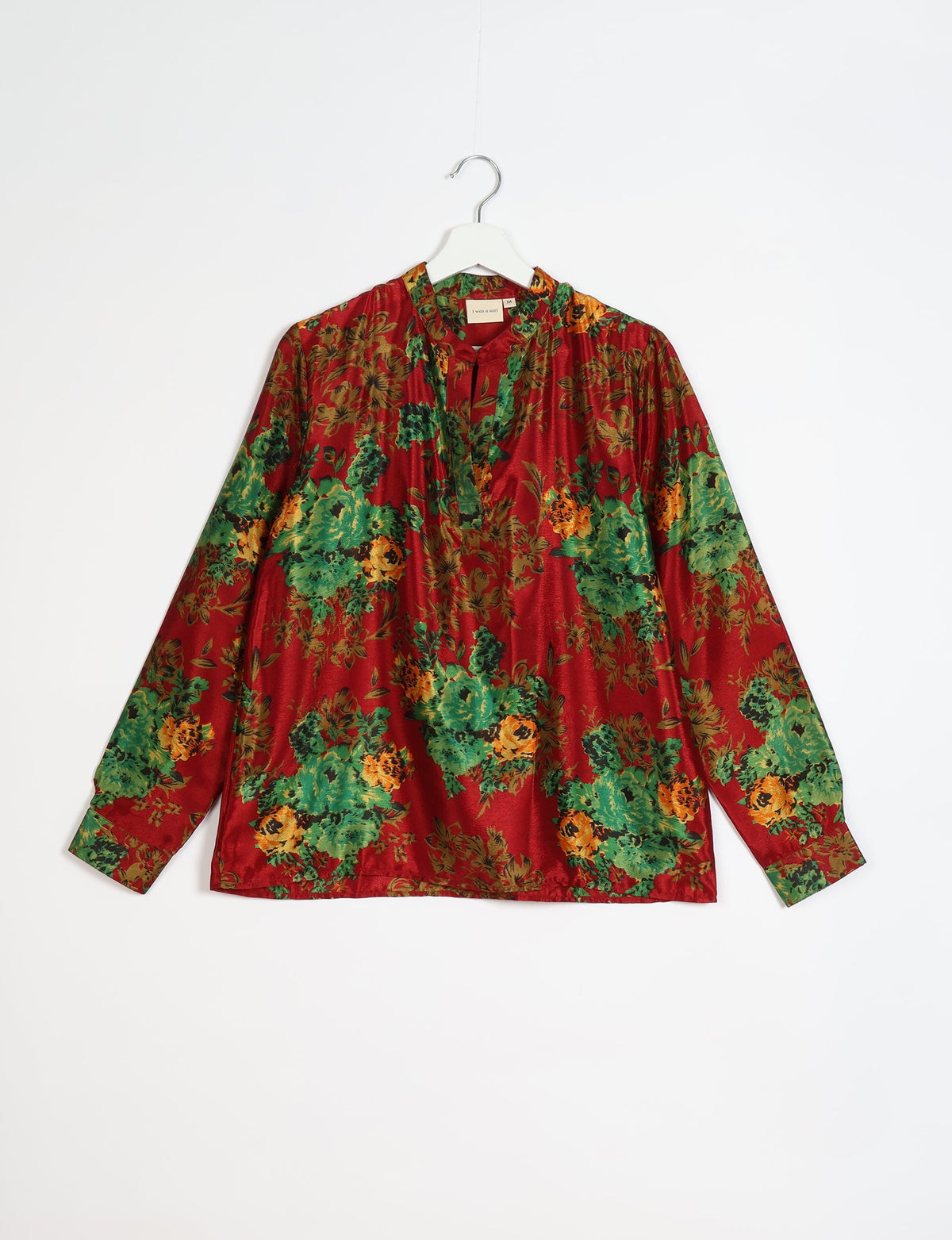 Red blouse with green and orange floral print, long sleeves, and a split neckline, hanging on a white hanger