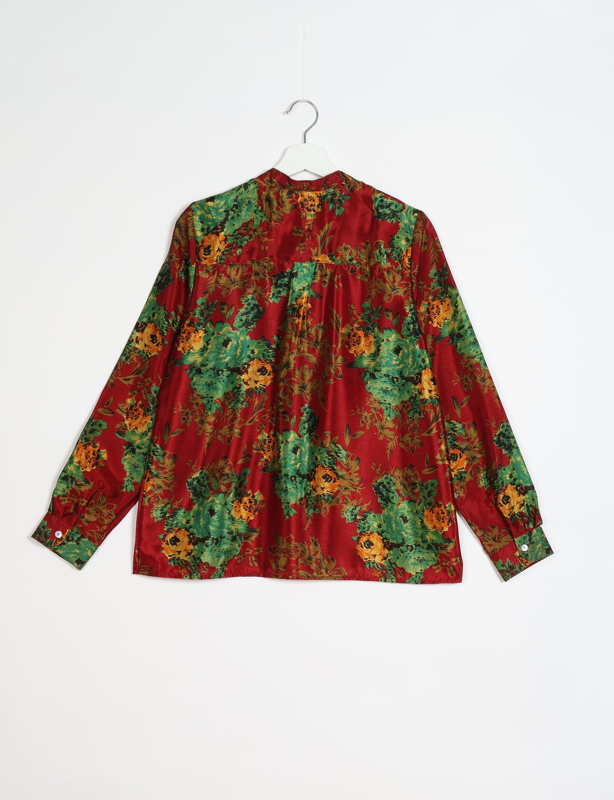 Red blouse with green and orange floral print, long sleeves, buttoned cuffs, shown from back on white hanger