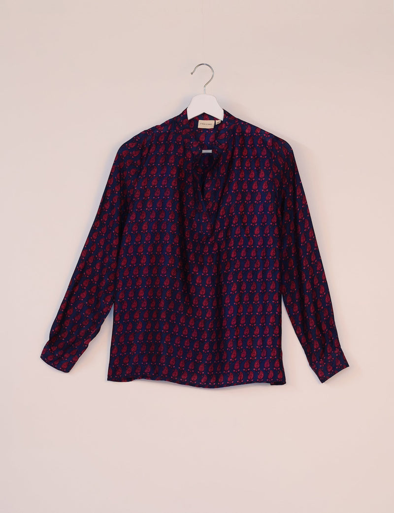Long-sleeve blue blouse with red paisley micro design, collarless neckline, hanging on white hanger against pale background