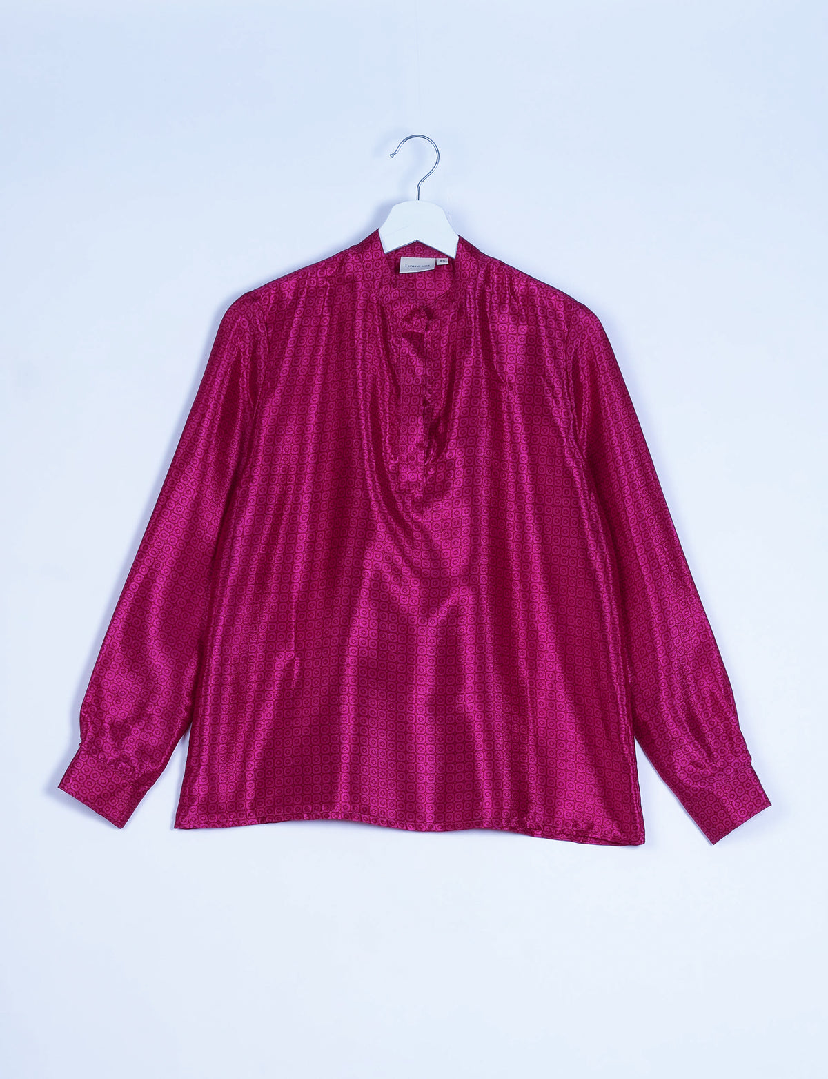 Pink long-sleeve blouse with micro geometric pattern, gathered neckline, and buttoned cuffs, hanging on white hanger