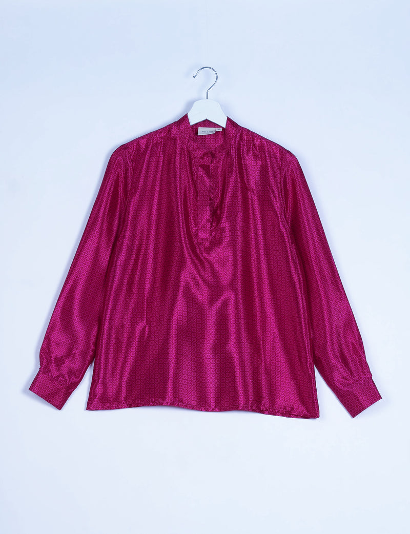 Pink long-sleeve blouse with micro geometric pattern, gathered neckline, and buttoned cuffs, hanging on white hanger