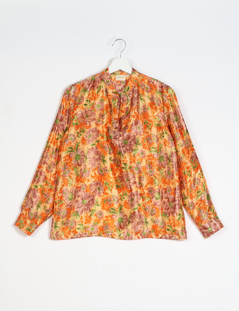 Yellow floral long-sleeve blouse with orange and green flower print, V-neck, and buttoned cuffs, hanging on white hanger