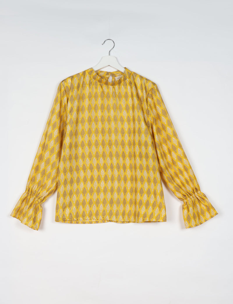 Yellow blouse with beige leaf diamond pattern, long gathered sleeves with ruffle cuffs, round neckline, hanging on white hanger