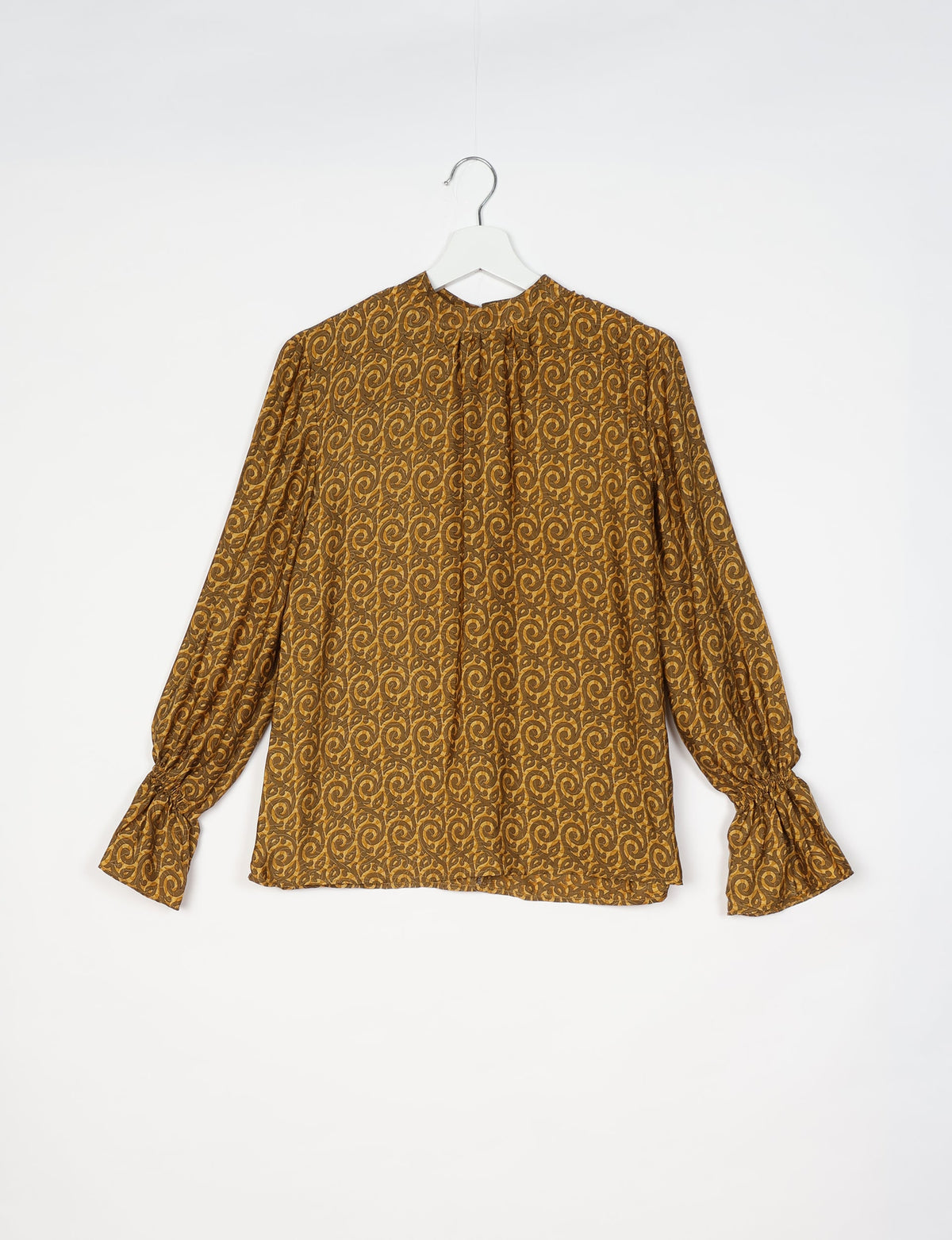 Long-sleeve blouse with yellow and brown abstract swirl pattern, gathered neckline, and ruched cuffs, hanging on white hanger