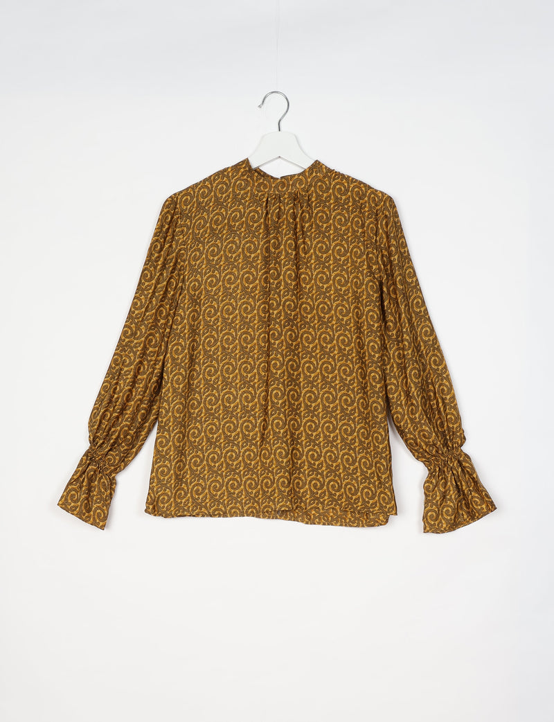 Long-sleeve blouse with yellow and brown abstract swirl pattern, gathered neckline, and ruched cuffs, hanging on white hanger