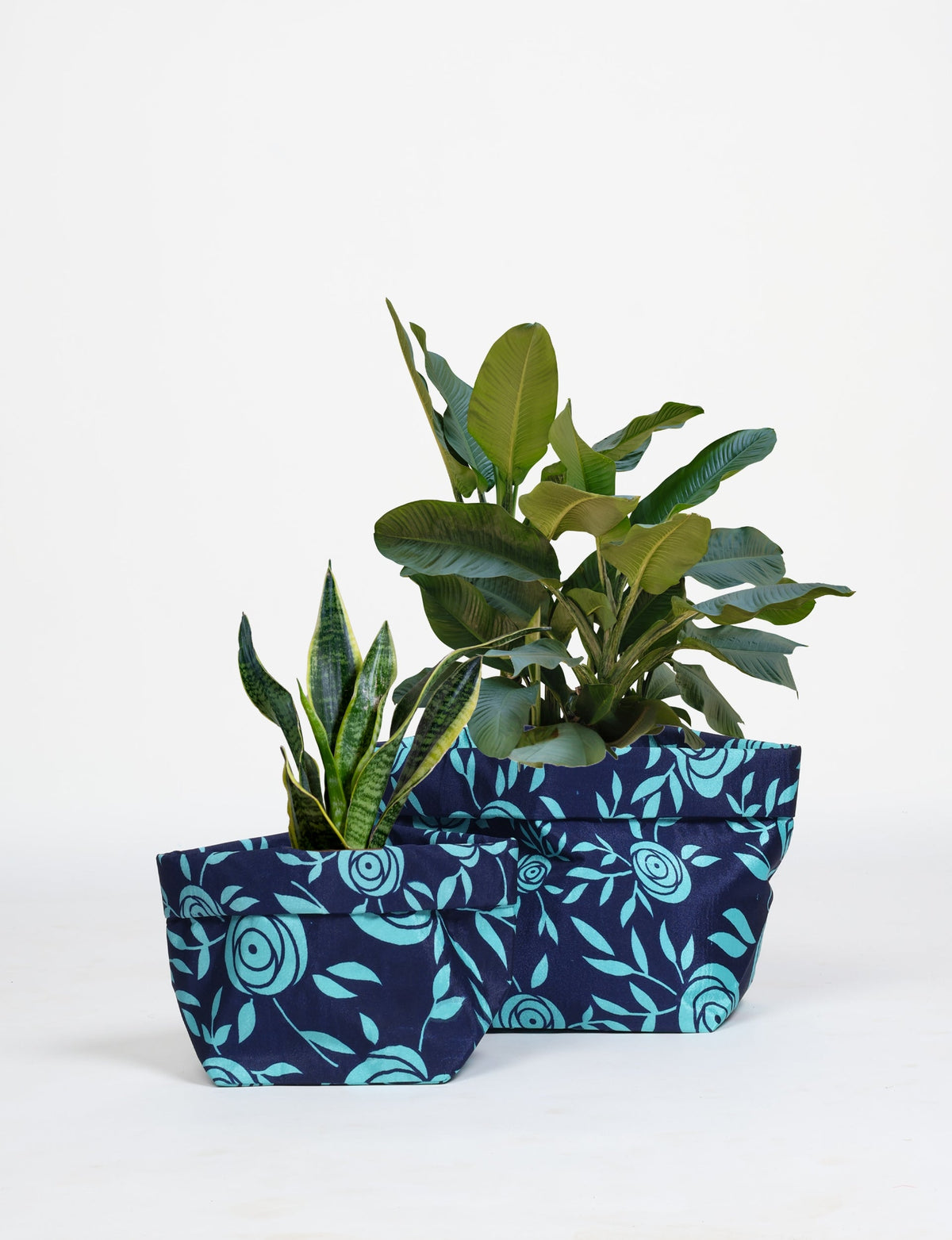 Two blue floral fabric plant pot covers with waterproof lining, shown with green plants, in small and medium sizes
