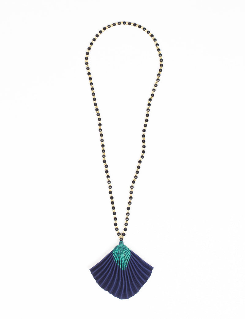 Necklace with black and gold beads and a pleated blue fabric pendant with green abstract pattern, flat lay on white background