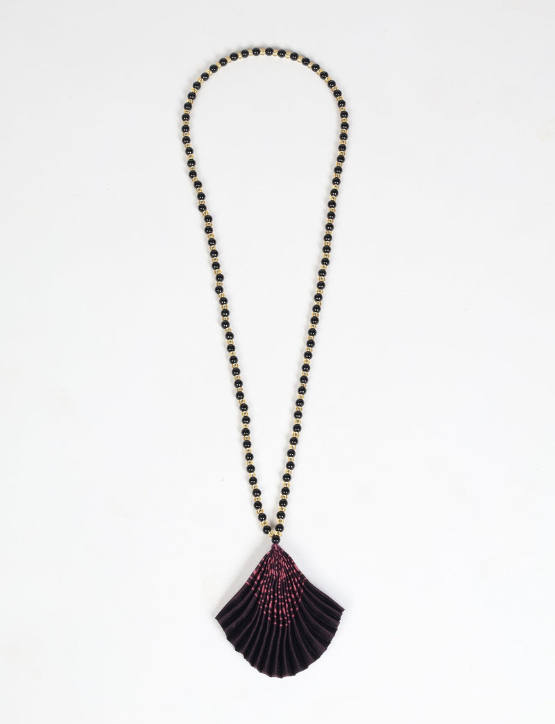 Necklace with black and gold beads and a pleated dark purple fabric pendant with pink abstract pattern, flat lay