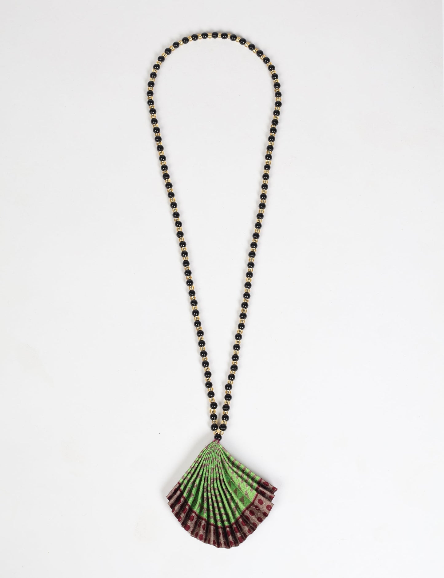 Dive into sustainable fashion with our PLEATED NECKLACE, a creation by talented female artisans in Mumbai. The pleated fan pendant, made from upcycled saris, hangs on a colorful necklace crafted from glass beads, embellished with sparkling glass crystals. An ethical, green fashion statement for conscious styling.