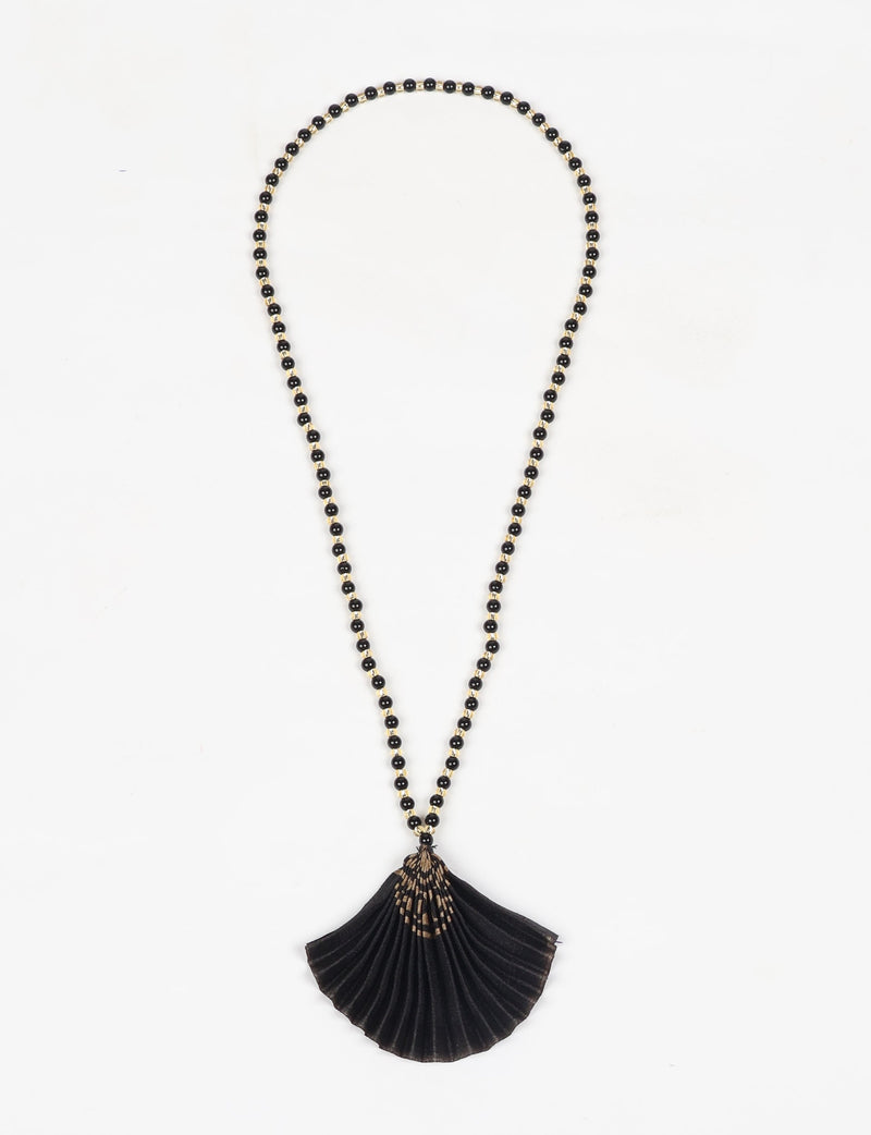 Black beaded necklace with a pleated black fabric pendant featuring an abstract beige pattern, flat lay on white background