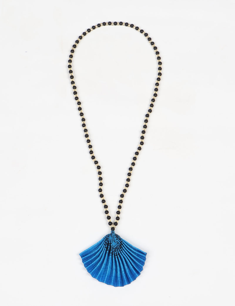 Necklace with black and gold beads and a pleated blue abstract fan-shaped pendant, flat lay on white background