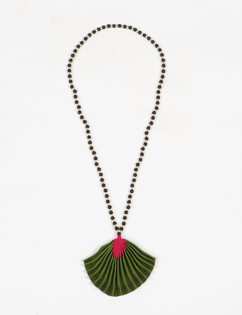 Necklace with black and gold beads and a pleated green pendant with a pink abstract design, flat lay on white background