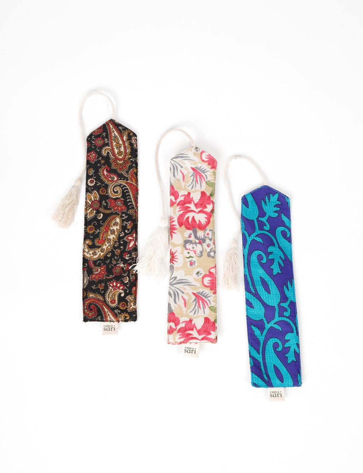 Set of three fabric bookmarks with tassels, featuring black paisley, beige floral, and blue leaf patterns, flat lay view