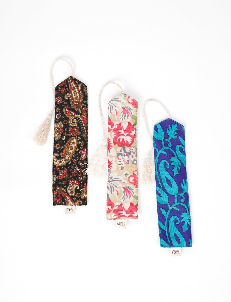 Set of three fabric bookmarks with tassels, featuring black paisley, beige floral, and blue leaf patterns, flat lay view