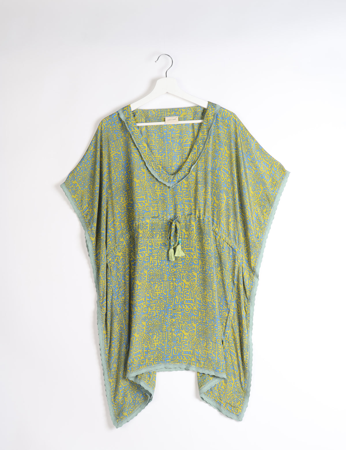Short green kaftan with abstract blue pattern, lace trim on edges, V-neckline, and tassel tie at waist, hanging on white