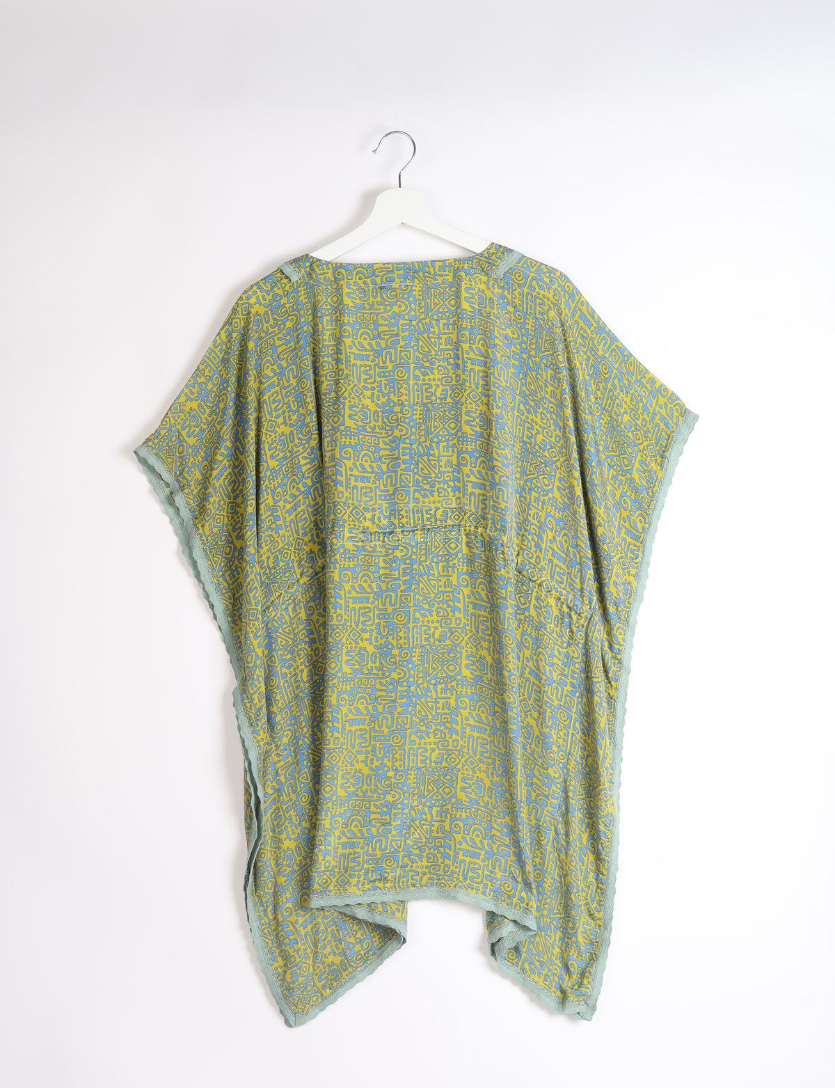 Short kaftan with green and blue abstract pattern, lace trim on edges, shown hanging on white hanger, back view