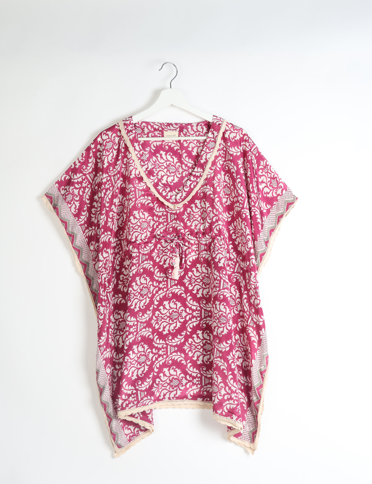 Pink tropical short kaftan with white floral pattern, lace trim, V-neck, and drawstring waist, hanging on white hanger