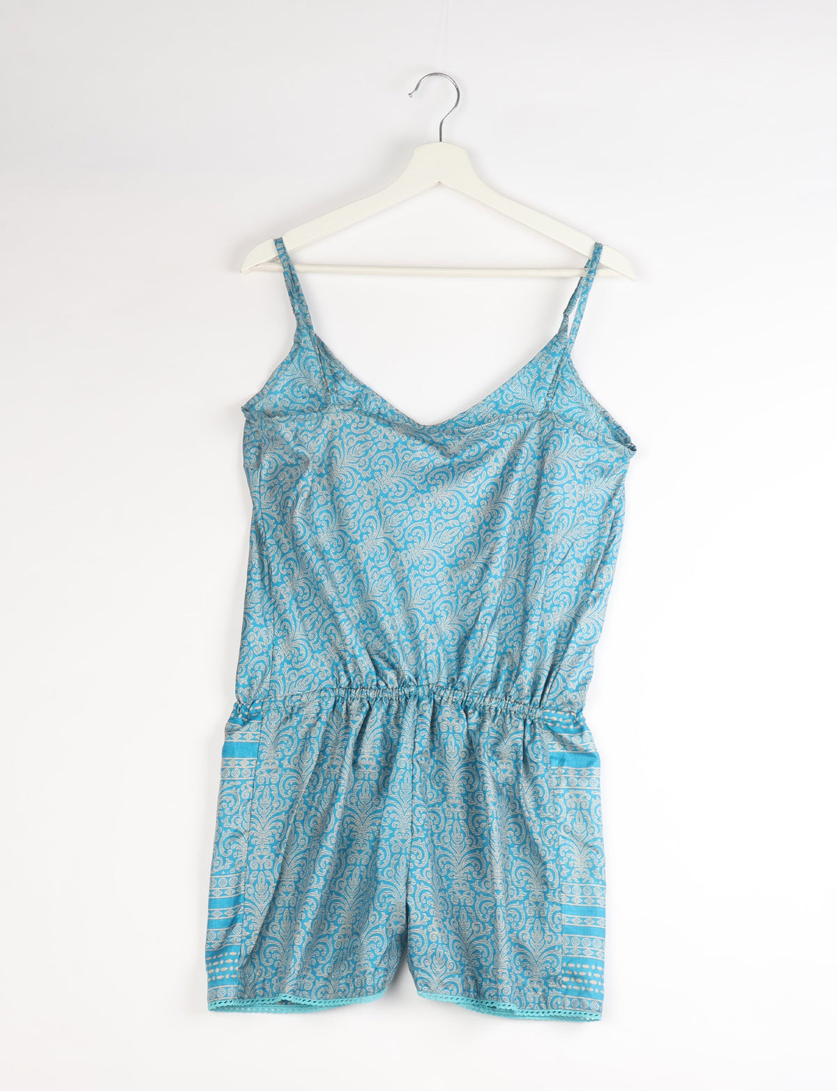 Blue playsuit with white abstract paisley pattern, adjustable spaghetti straps, elastic waist, and lace trim on hem, hanging