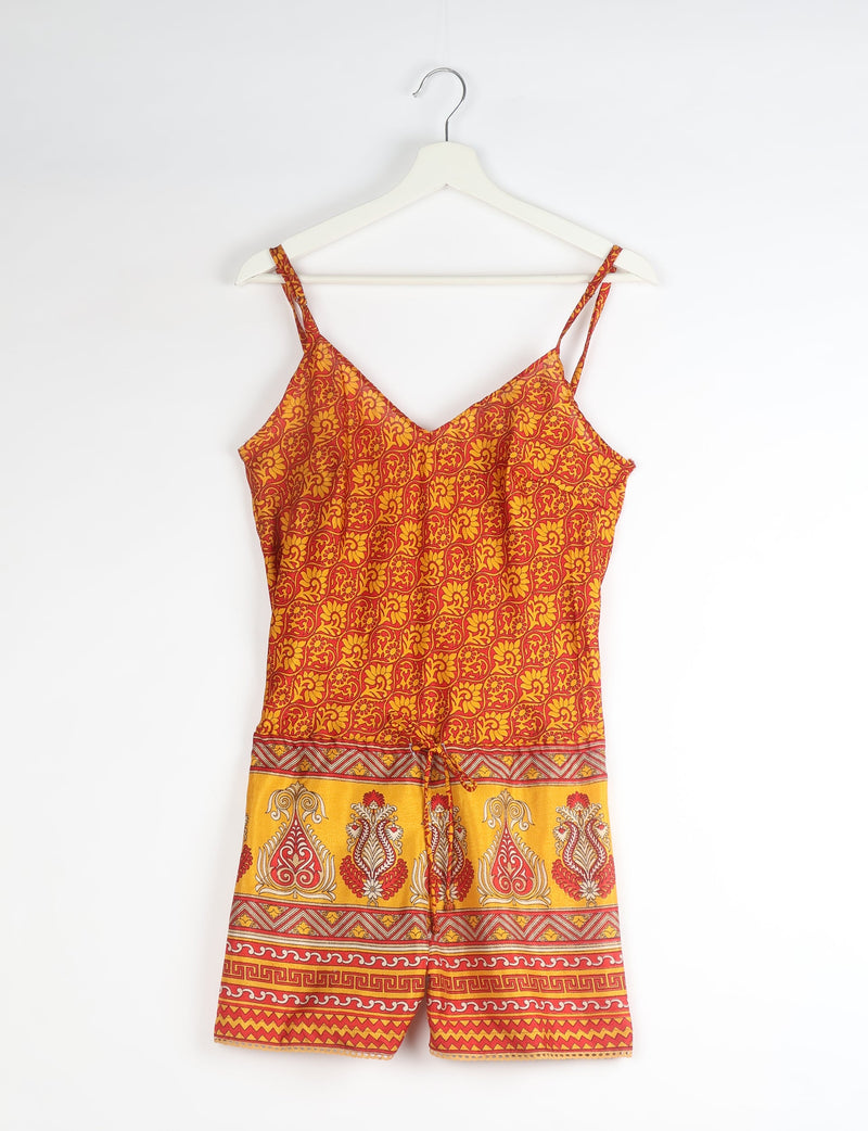 Orange and red abstract patterned playsuit with thin straps and a drawstring waist, hanging on a white hanger