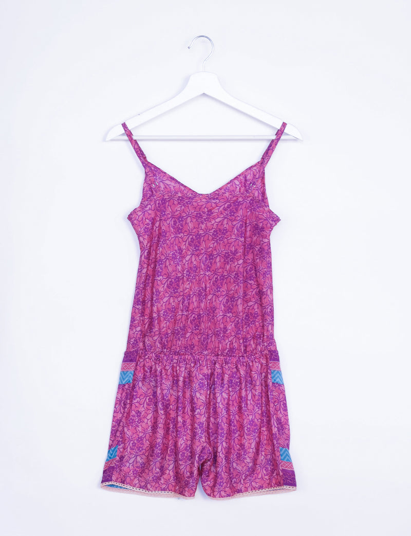Pink tropical playsuit with lace trim and adjustable straps hanging on a white hanger against a white background
