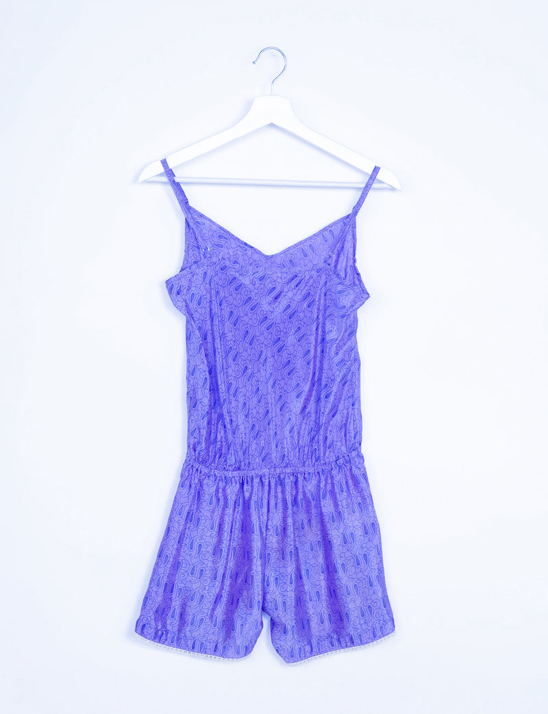 Purple playsuit with micro paisley design, lace trim, adjustable spaghetti straps, and elastic waist, hanging on white hanger