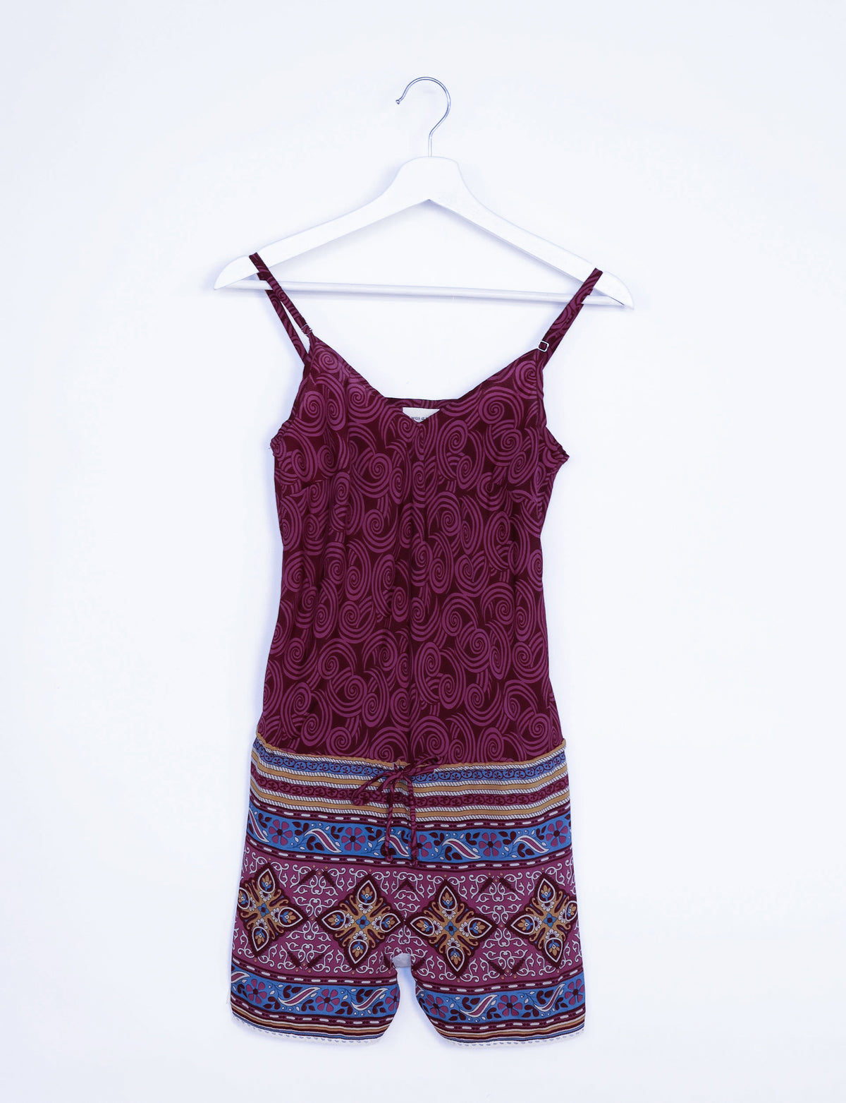 Red playsuit with abstract swirl pattern on top and multicolor geometric border print on shorts, hanging on white hanger
