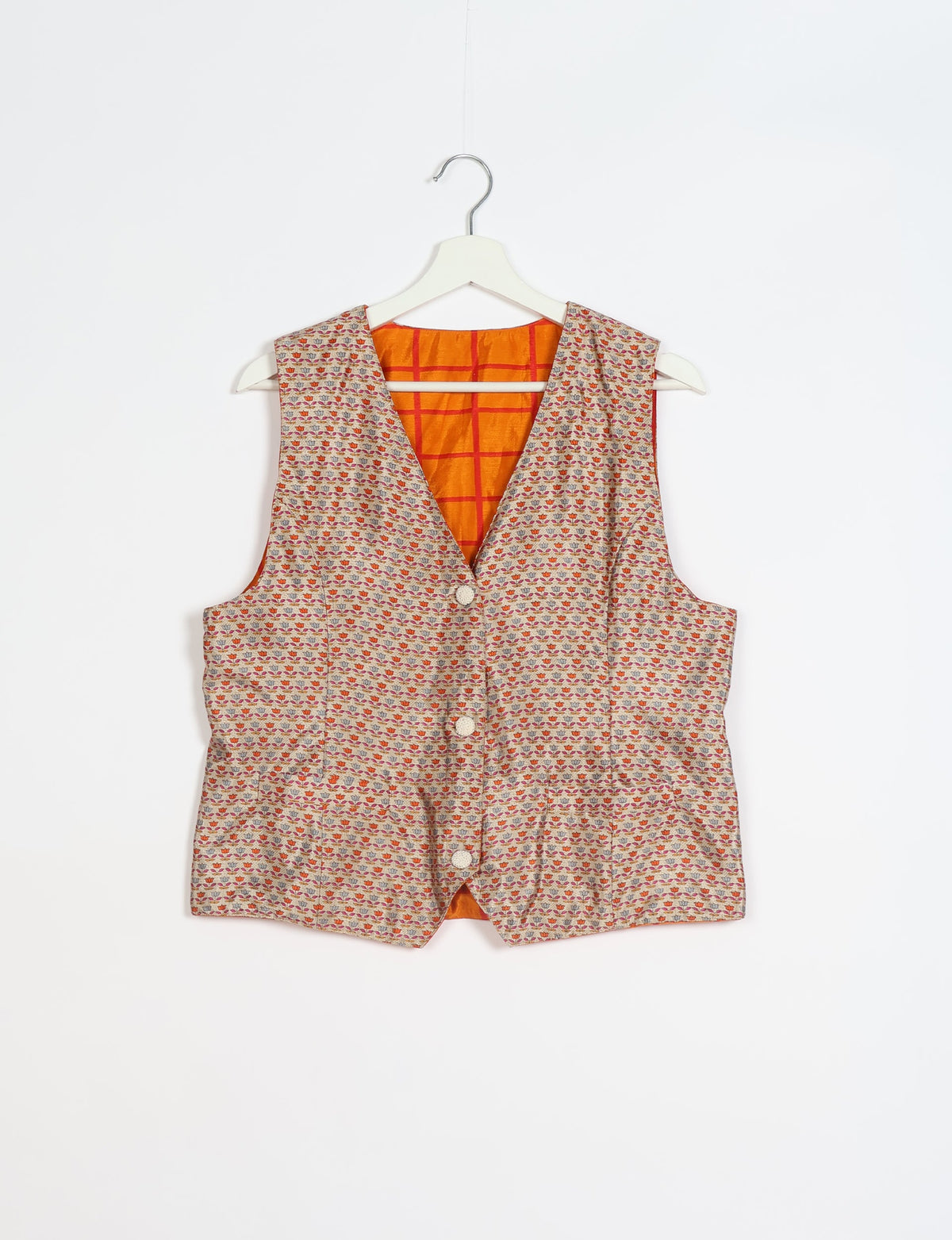 Beige waistcoat with small multicolor floral pattern, front buttons, and orange checkered inner lining, hanging on white hanger