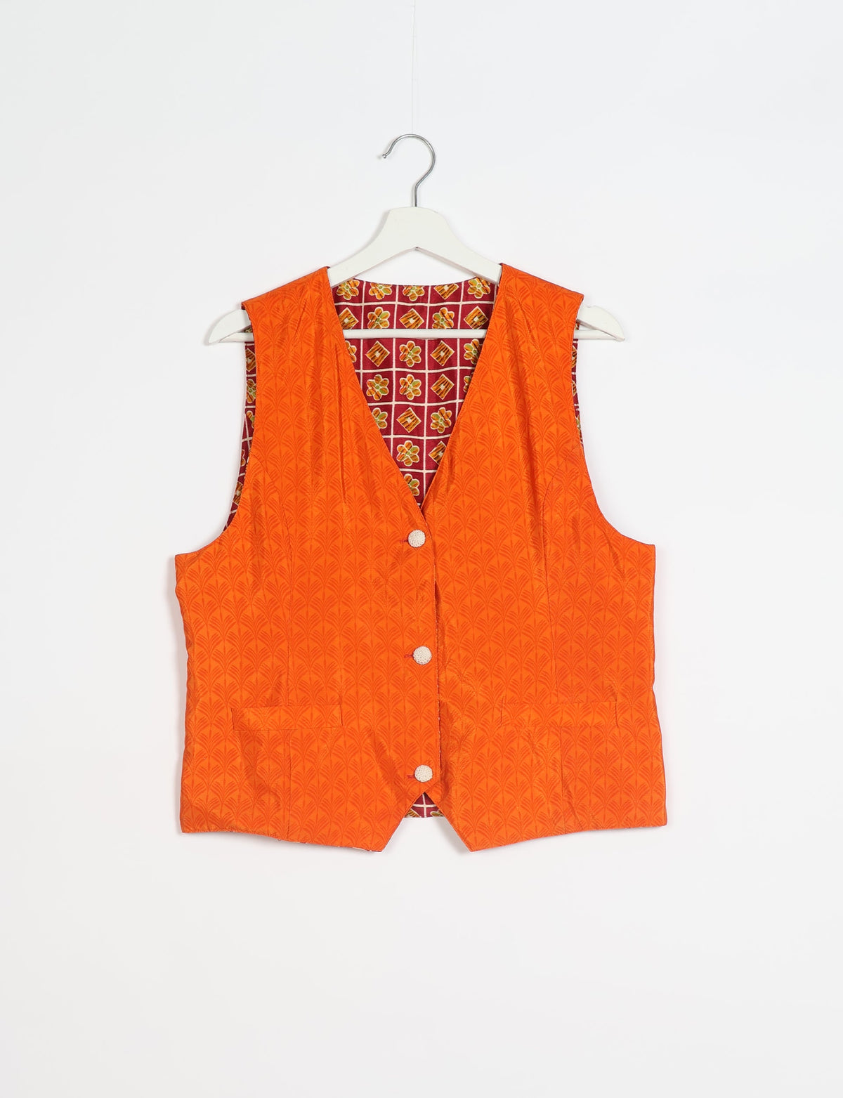 Orange sleeveless waistcoat with textured leaf pattern, front buttons, and floral patterned inner lining, hanging on white hanger