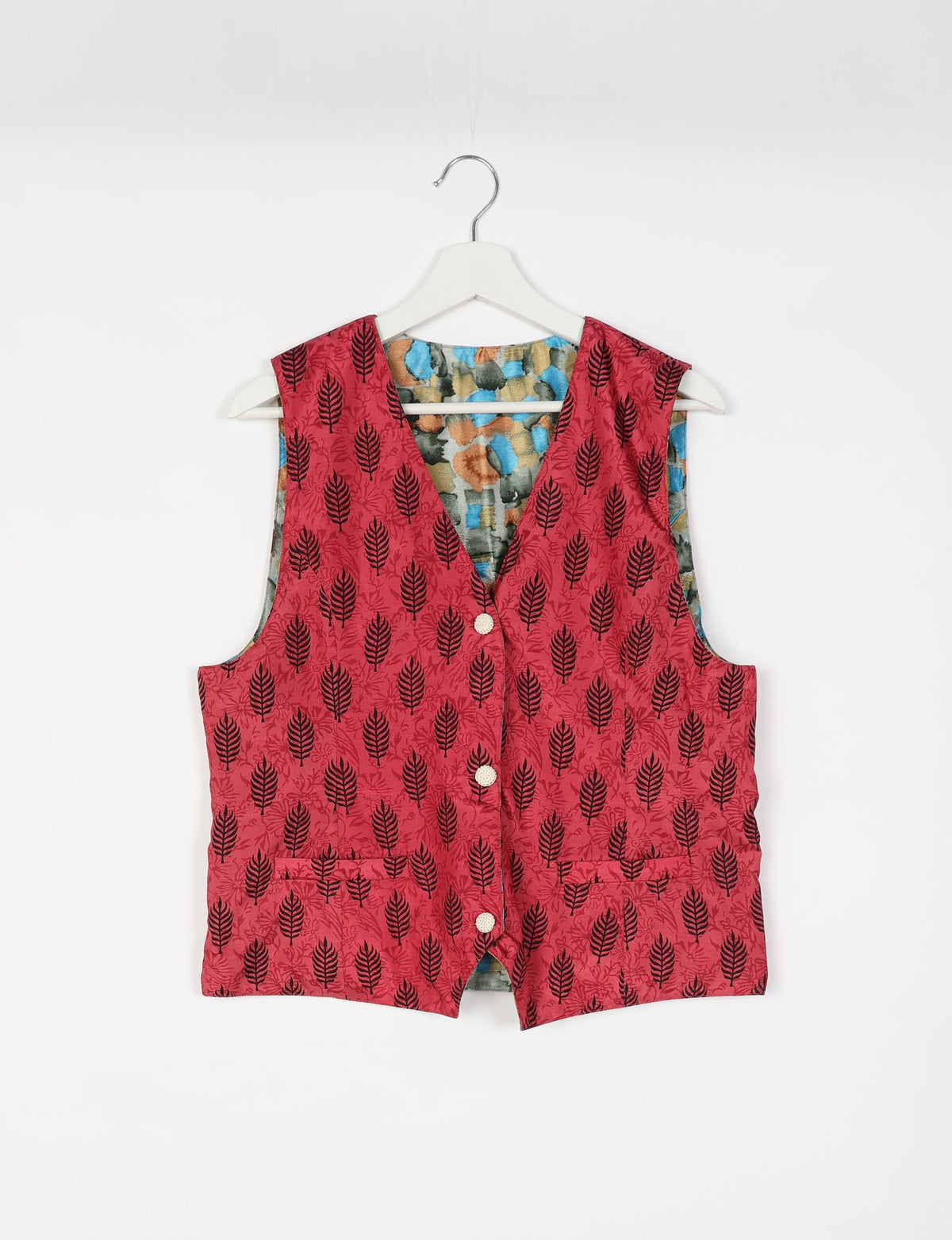 Pink sleeveless waistcoat with black leaf pattern, front buttons, and two front pockets, hanging on white hanger, front view