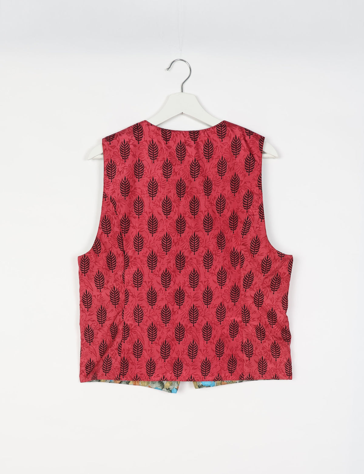Pink sleeveless waistcoat with black leaf pattern hanging on white hanger against white background