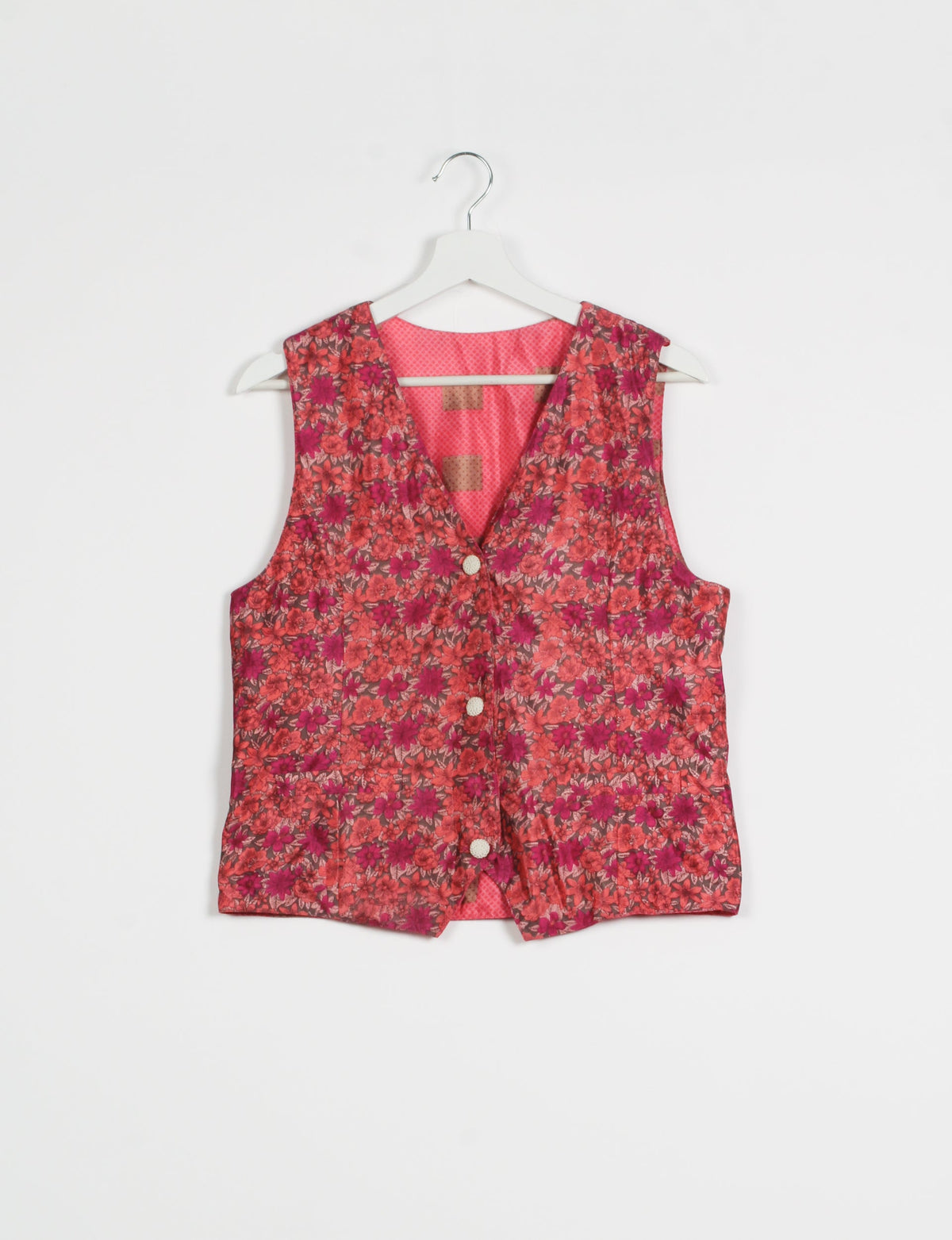 Pink floral sleeveless waistcoat with front buttons, V-neckline, and contrasting pink patterned lining, hanging on white hanger