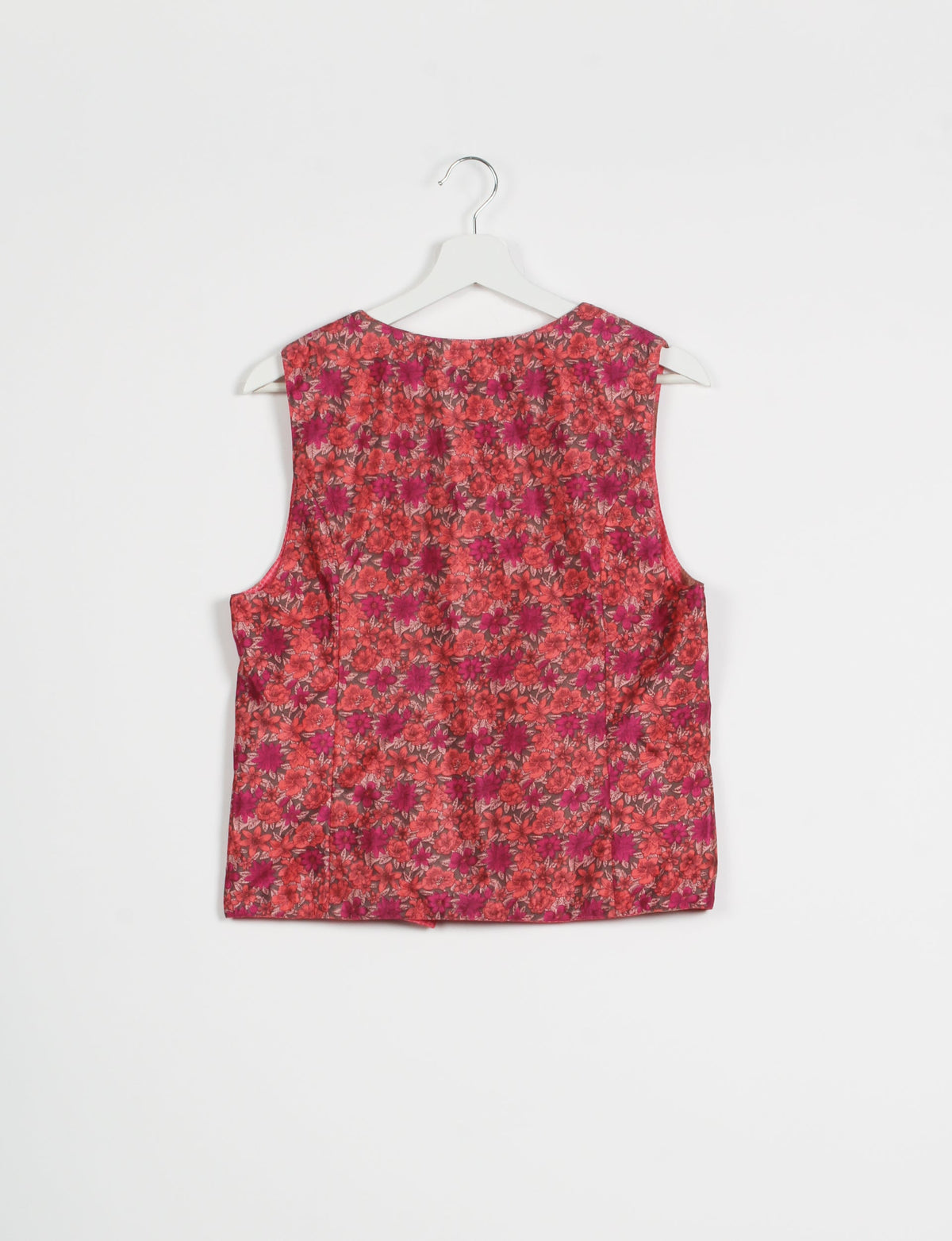 Pink floral sleeveless waistcoat hanging on white hanger, back view, with red and magenta flower pattern on fabric