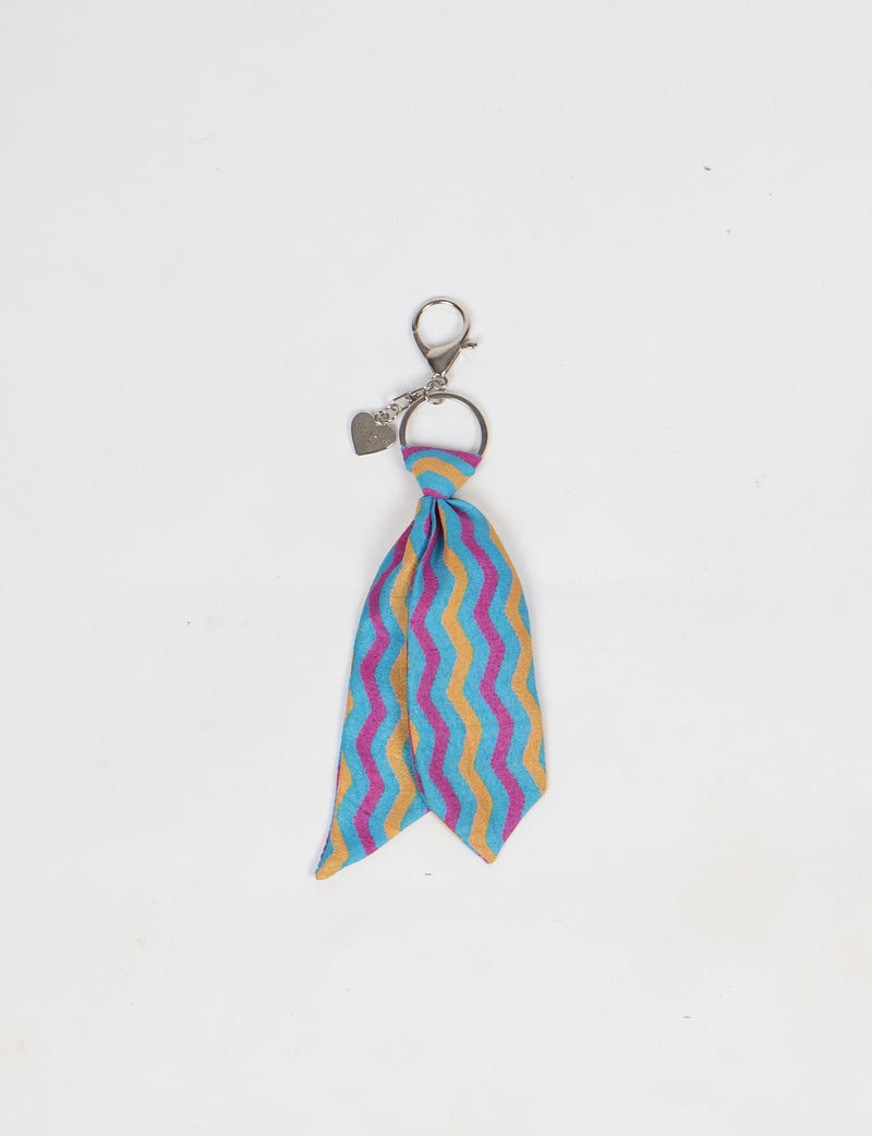 Blue, yellow, and pink wavy striped fabric tie keychain with silver ring and heart-shaped charm on white background