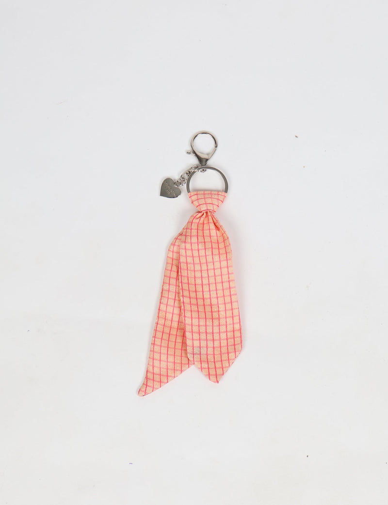 Pink geometric patterned fabric tied as a miniature necktie on a silver keyring with a heart-shaped charm, flat lay