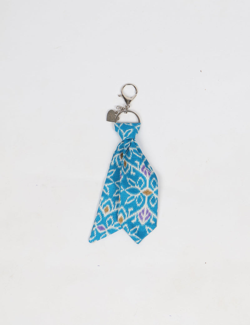 Blue floral patterned fabric tie keychain with silver metal clasp and small heart-shaped charm, flat lay on white background
