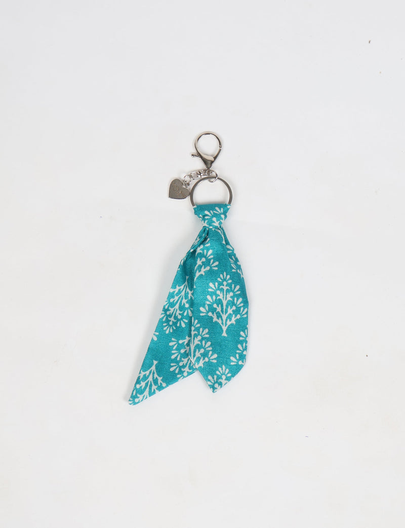 Blue floral fabric tie keychain with silver metal ring and heart-shaped charm, flat lay on white background