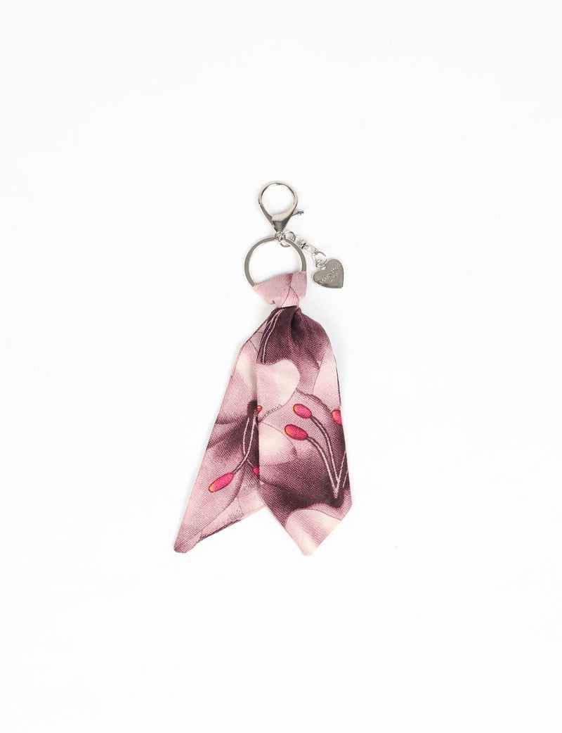 Silver keychain with pink floral fabric tied and a small heart-shaped charm attached, flat lay on white background