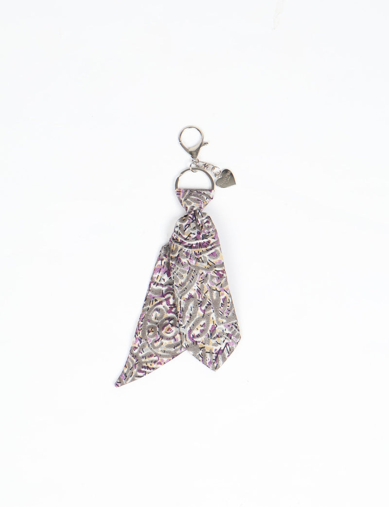 Grey abstract patterned fabric keychain with silver metal ring, lobster clasp, and small heart charm, flat lay on white background