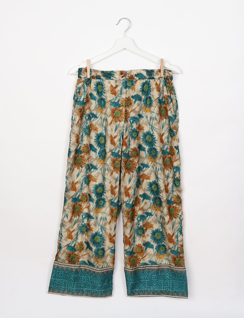 Beige floral lounge pants with teal and brown flower print and teal geometric border, hanging on white hanger front view