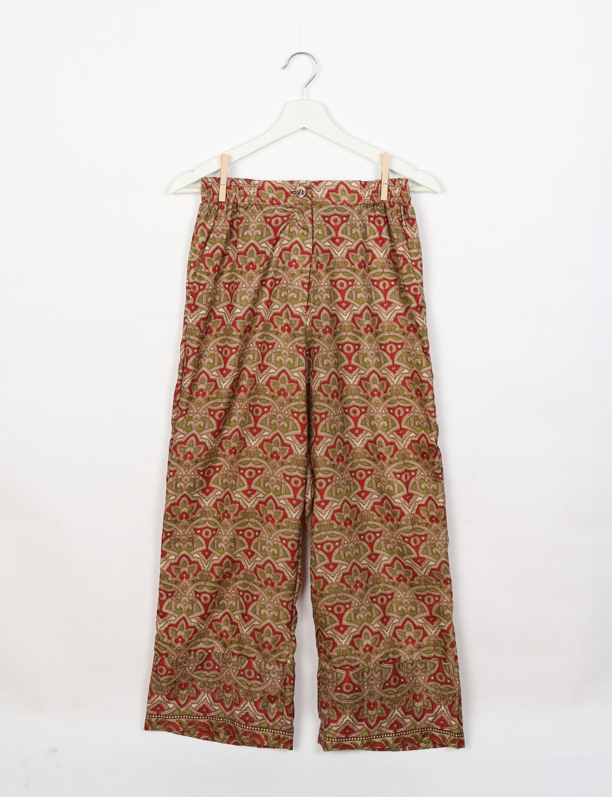 Beige tropical patterned lounge pants with button and elastic waistband, hanging on white hanger against white background