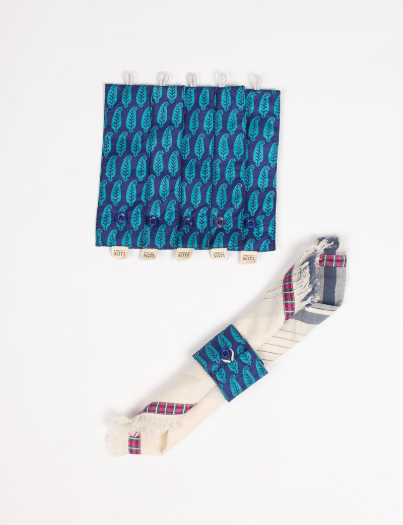 Set of six blue fabric napkin rings with teal leaf pattern, buttons, and "I was a sari" tags, shown flat and on a rolled napkin