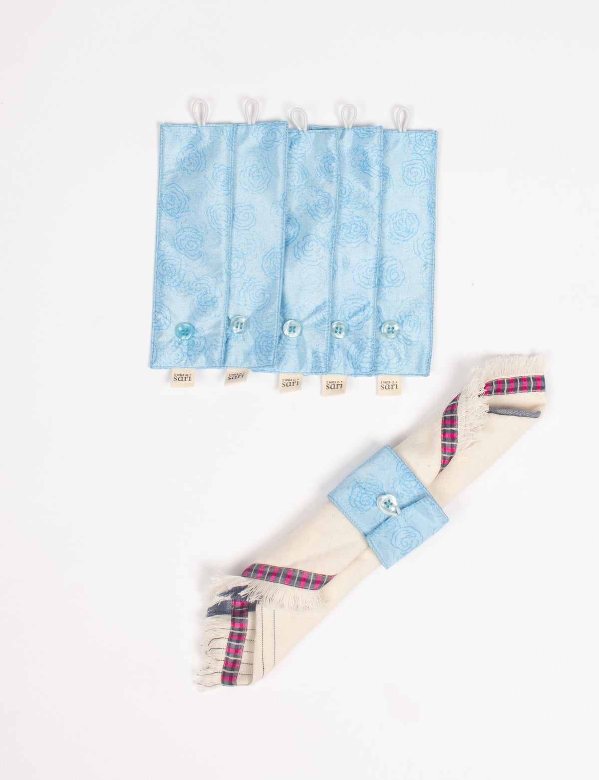 Set of six light blue fabric napkin rings with floral pattern, buttons, and "I was a sari" tags, shown flat and on a rolled napkin