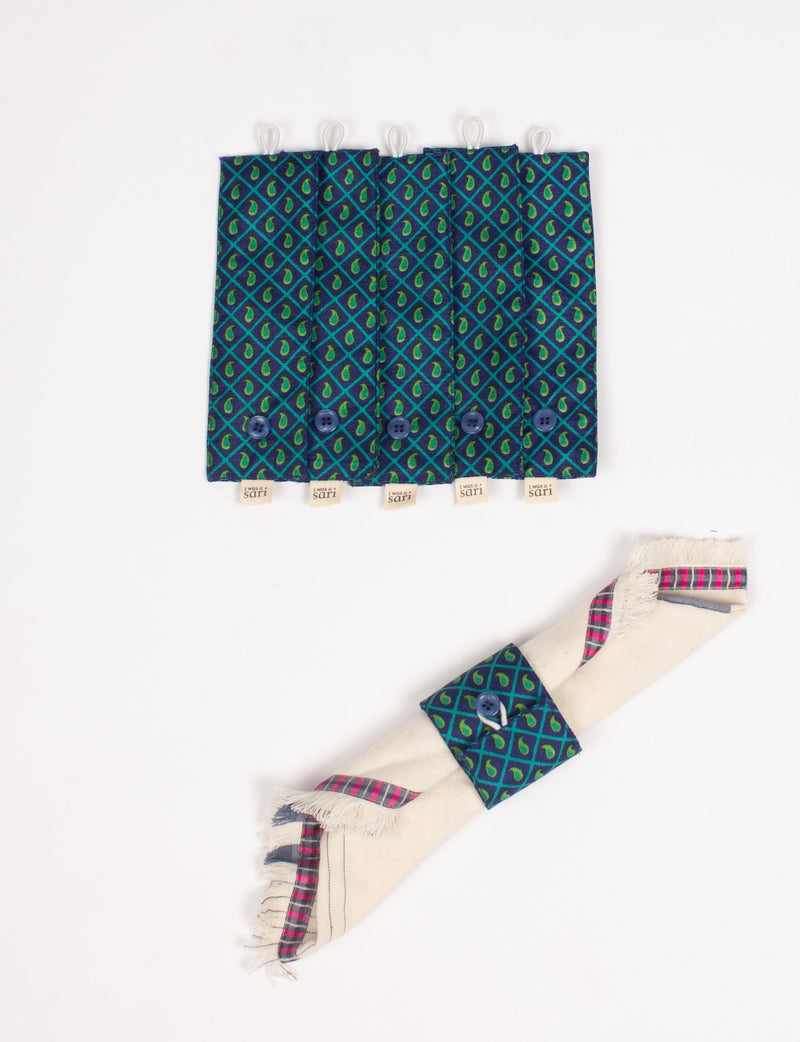 Set of six blue and green patterned fabric napkin rings with buttons and "I was a sari" tags, one shown wrapped on a napkin