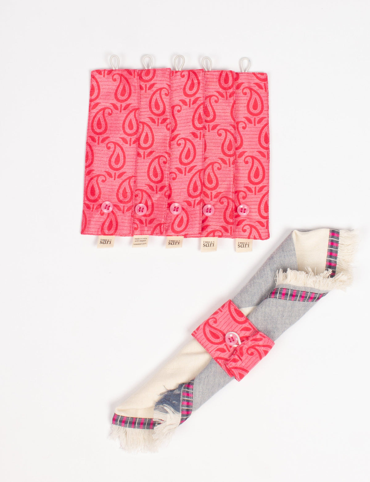 Set of six pink fabric napkin rings with red paisley pattern, buttons, and hanging loops, shown flat and on a folded napkin
