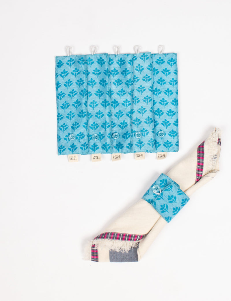 Set of six blue fabric napkin rings with floral pattern and button closure, one shown holding a folded napkin with plaid trim